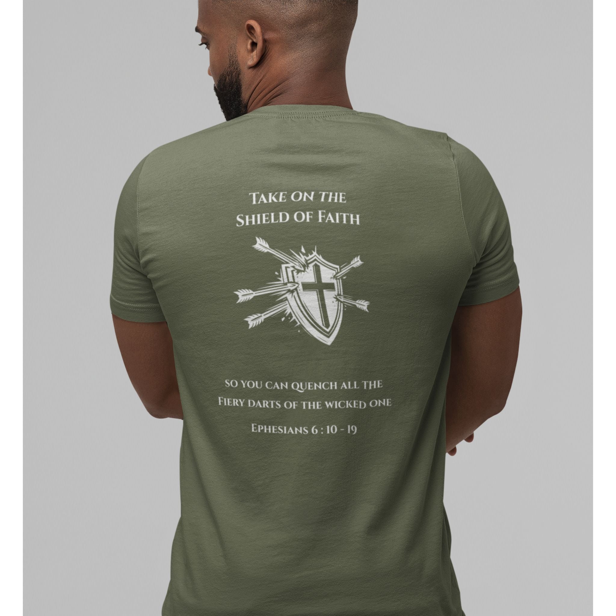 A man viewed from the back wearing an olive green t-shirt with a white graphic print featuring a shield, cross, and arrows, along with Bible verse text from Ephesians 6:10-17.