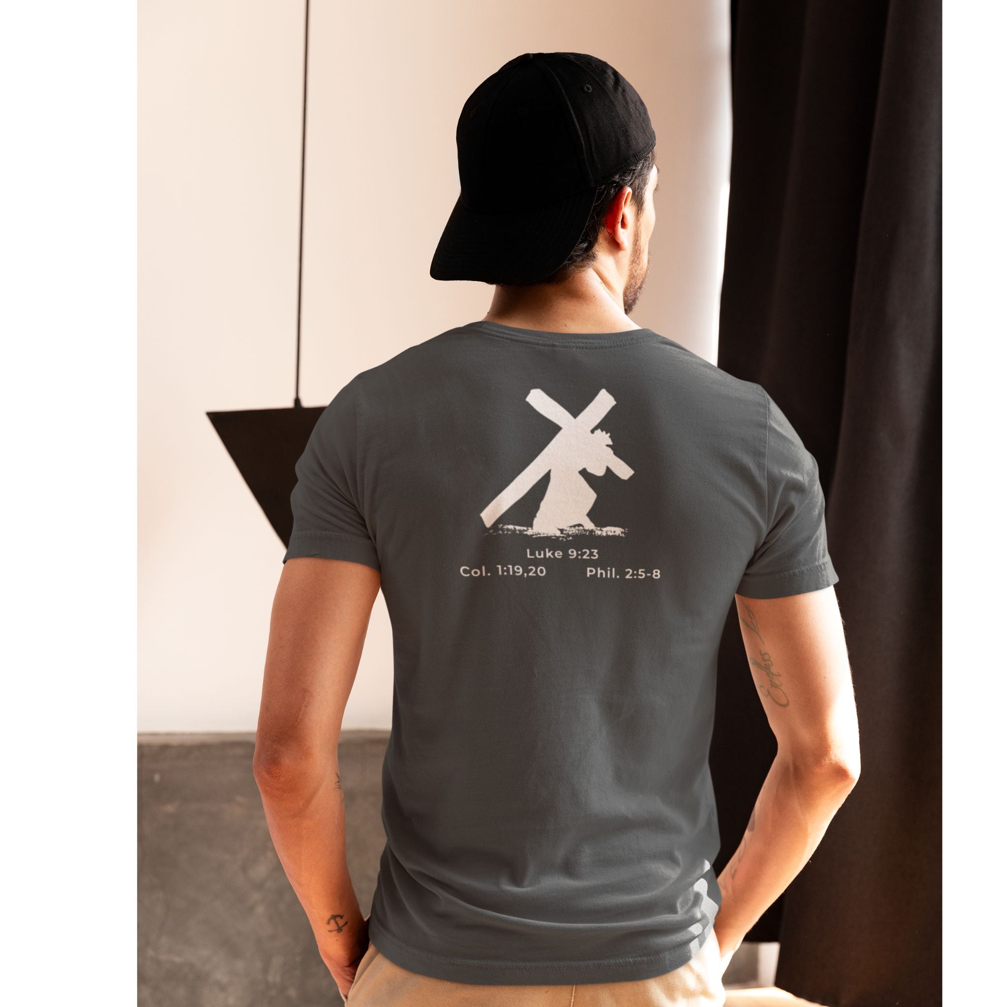 Person wearing a gray t-shirt with a design and text on the back, standing indoors.