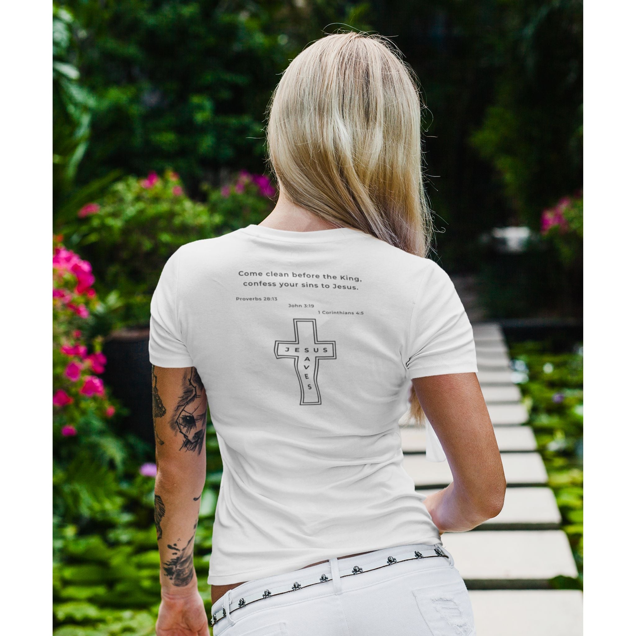 Person wearing a white t-shirt with text and a cross design, standing outdoors.