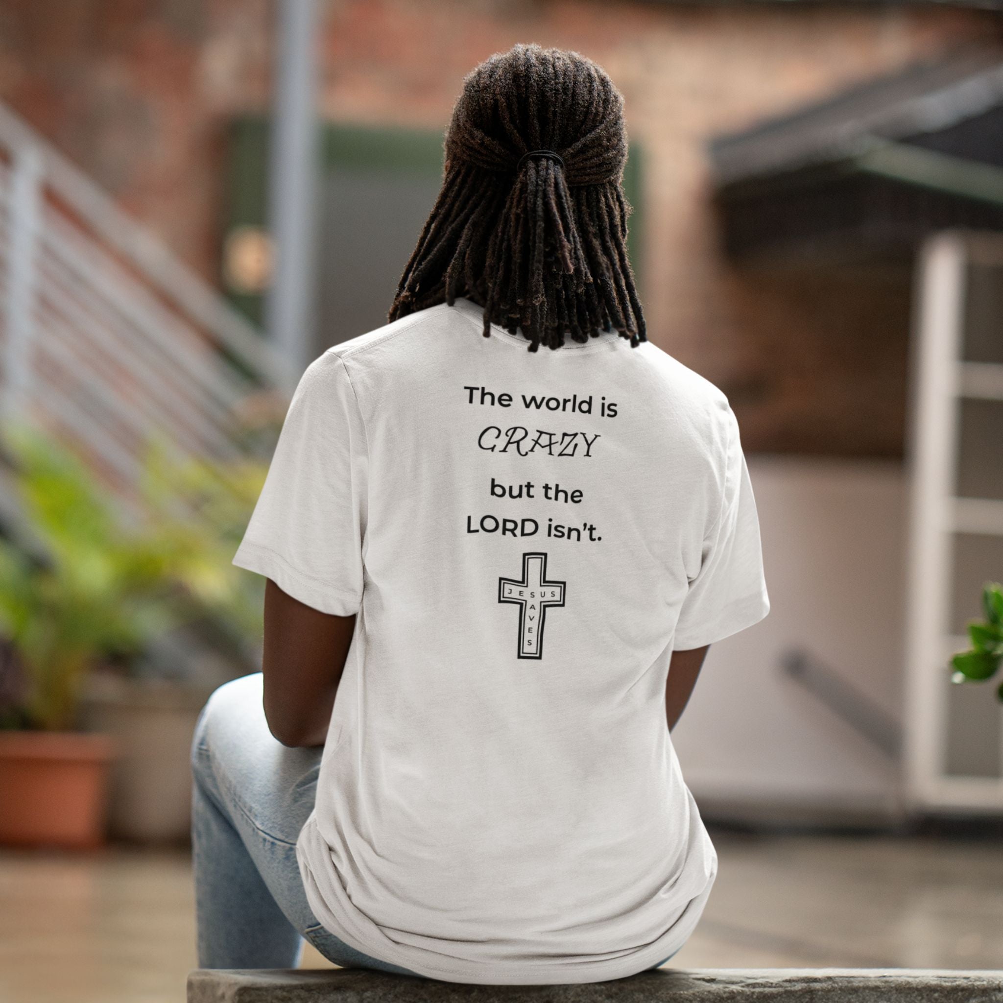 Back view of a white t-shirt with a black text design reading “The world is crazy but the Lord isn’t” and a small Jesus Saves cross detail.