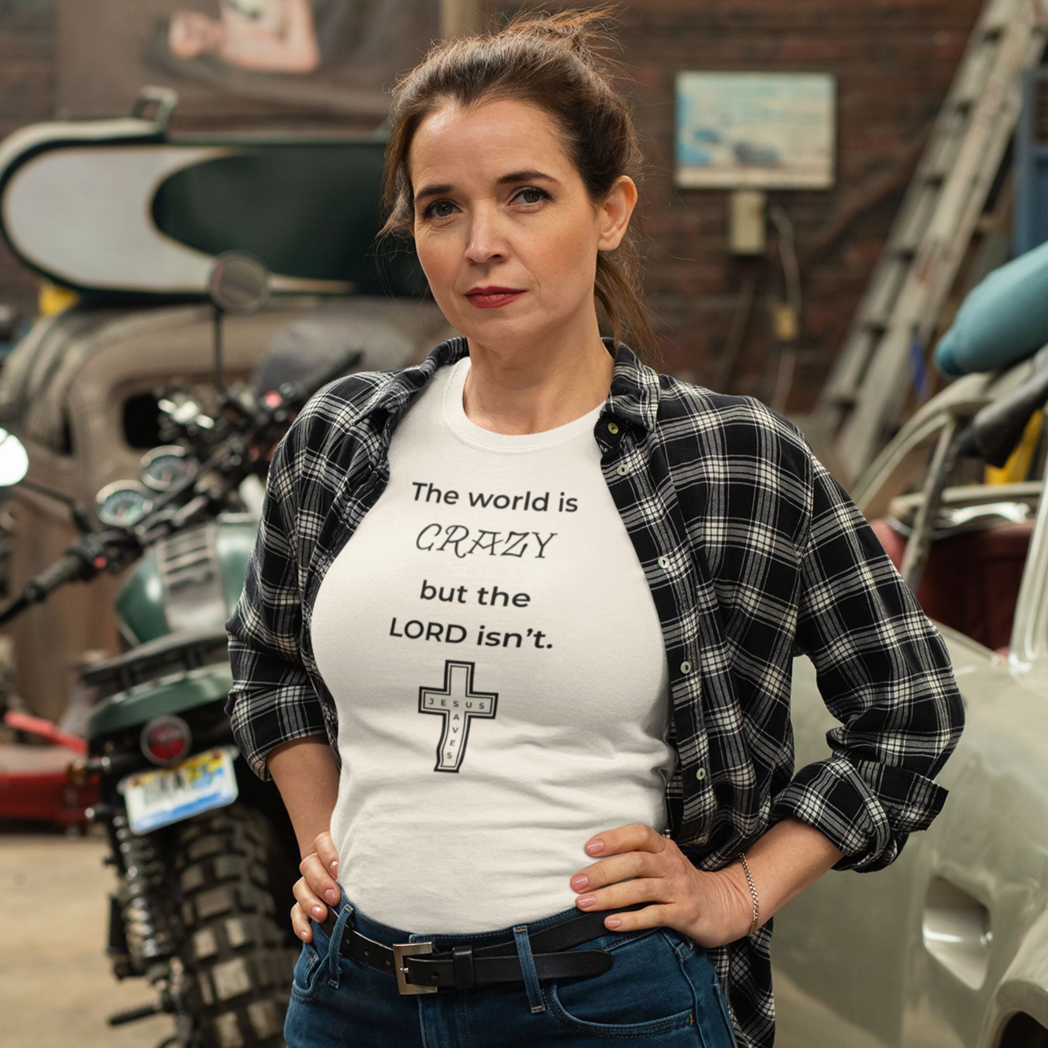Woman wearing a natural-colored t-shirt with a black text design, standing outdoors near vehicles and equipment.
