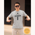 Christian t-shirt featuring the message "He Is Risen" arranged in the shape of a cross printed on the front.