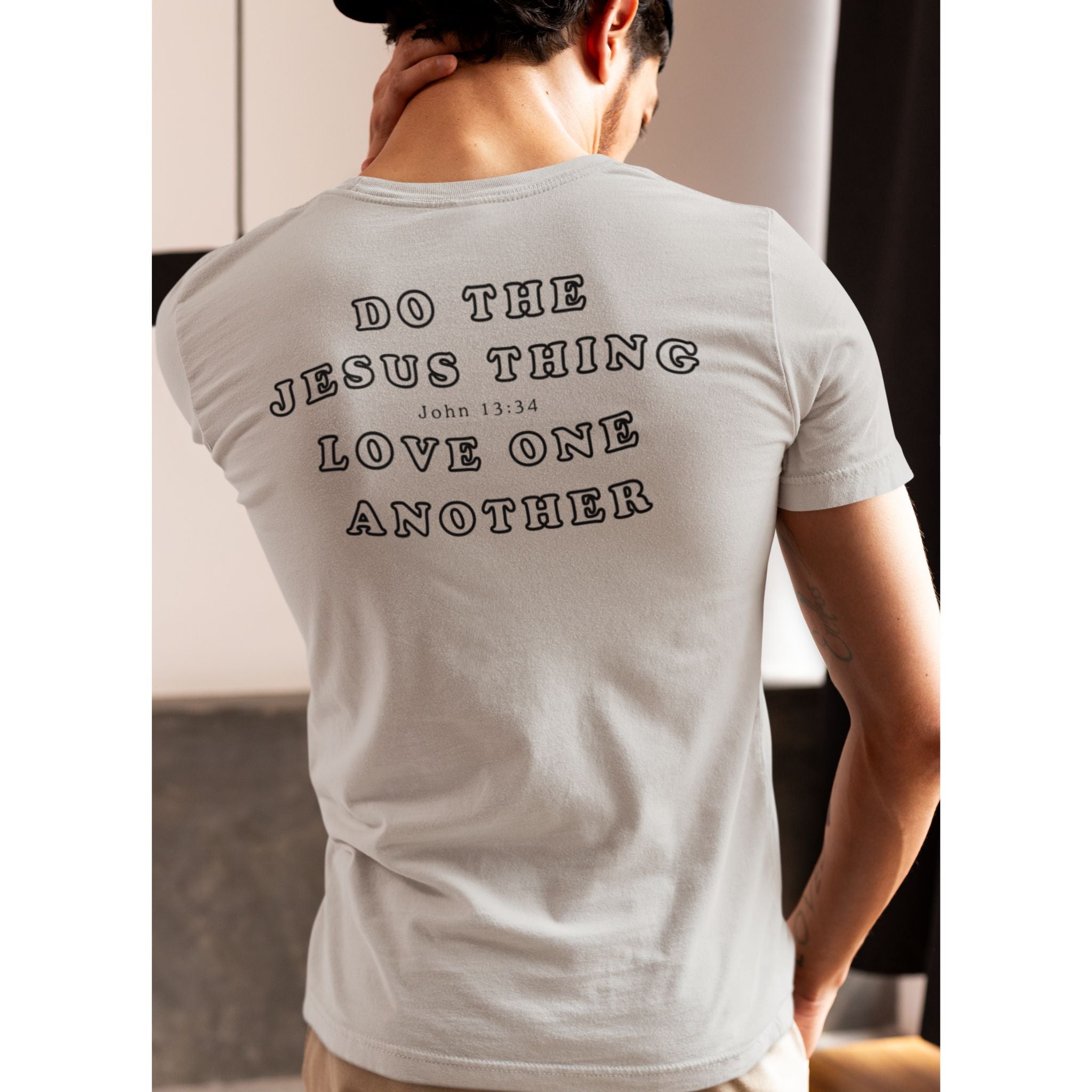A man wearing a light gray t-shirt, viewed from behind, showing the back graphic that reads 'DO THE JESUS THING LOVE ONE ANOTHER John 13:34' in black text.