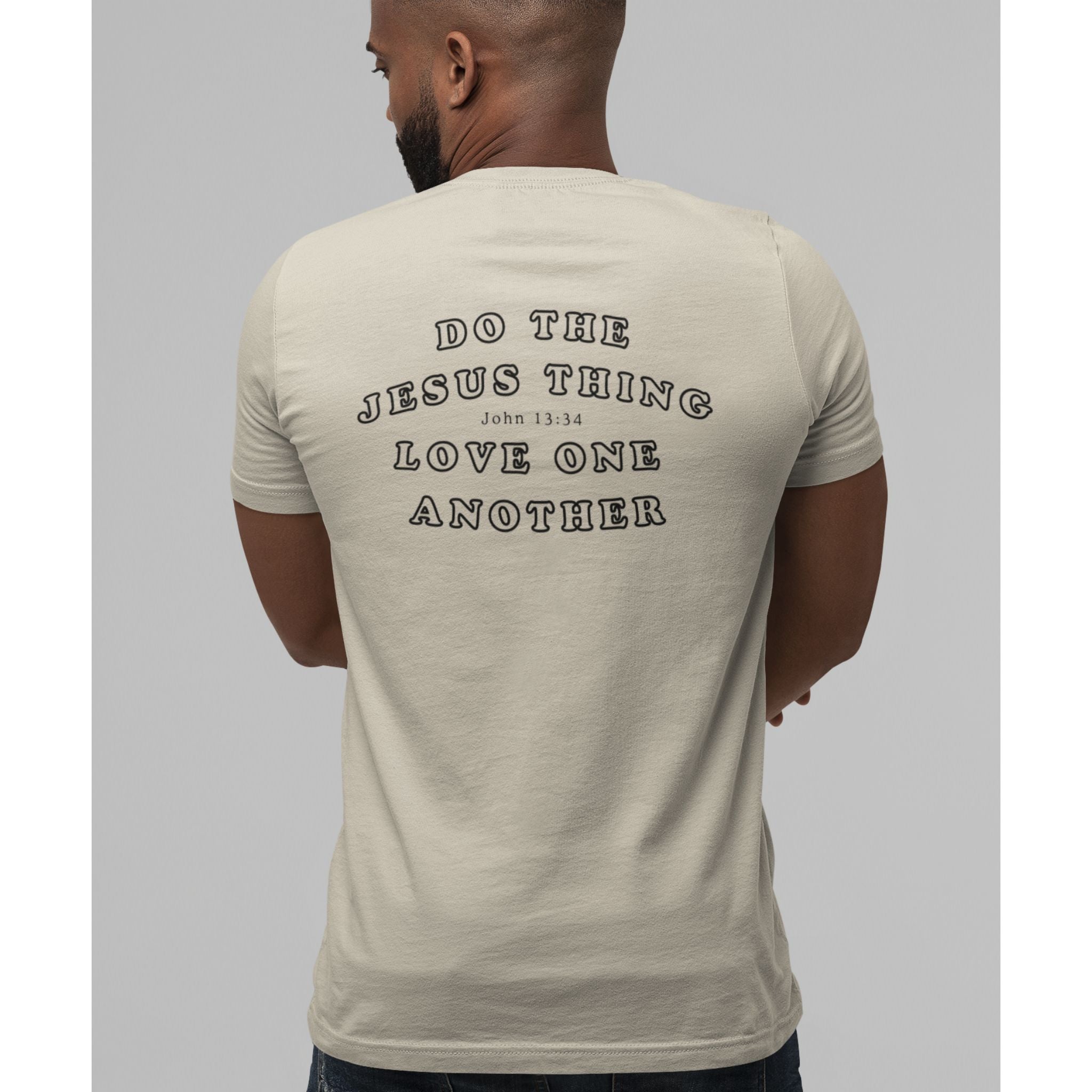 A man viewed from behind wearing a light beige t-shirt with black text on the back reading 'DO THE JESUS THING LOVE ONE ANOTHER' and 'JOHN 13:34'.