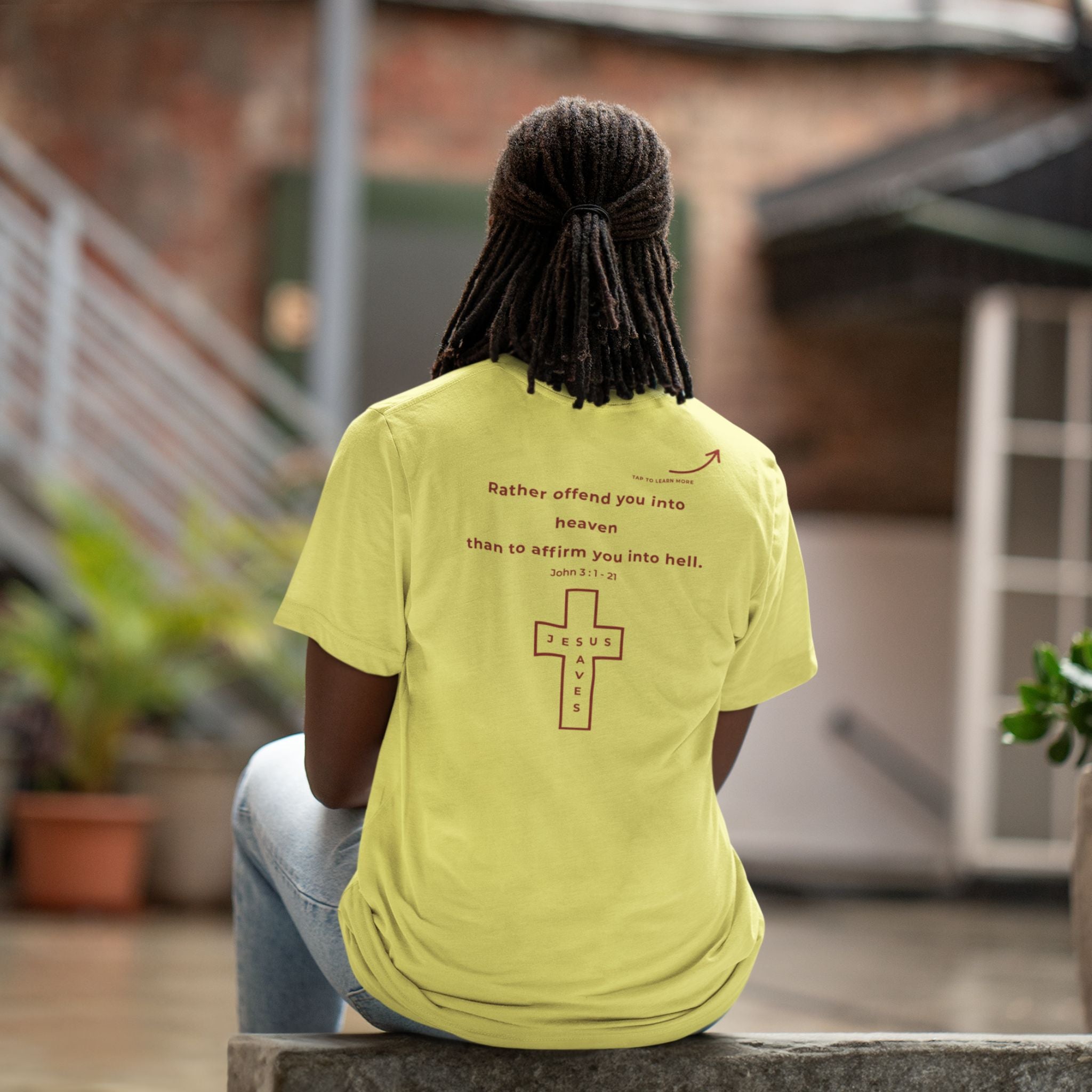 Back view of a seated person wearing a yellow Christian T-shirt with a red “Rather offend you into heaven than affirm you into hell” message and Jesus Saves cross.